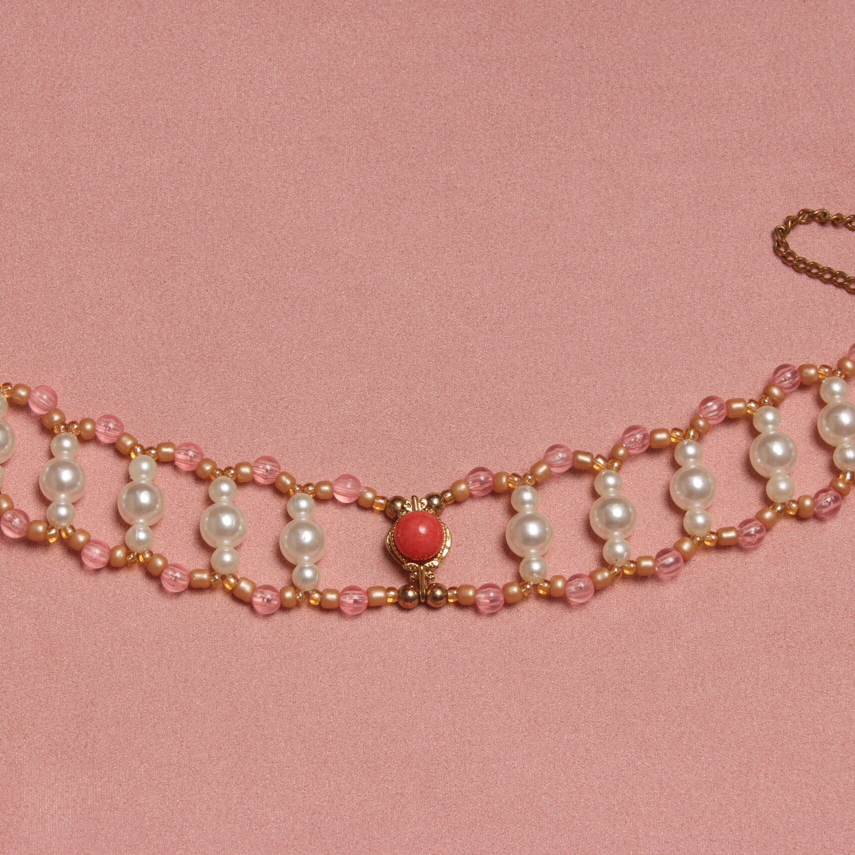 Collier ras le cou en perles vintage. 2 rangées de perles rose reliées entre elles par des petites rangées de 3 perles verticales blanches nacrées. Au centre il y a un pendentif doré orné d'une perle rose. Taille ajustable grâce à la chaînette dorée