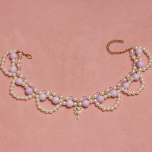 Collier en perles vintage. 2 rangées de perles blanches et parme, composées de petites perles pour la rangée la plus près du cou et de perles parme plus grosses pour la seconde rangée. Arcs de cercles en perles blanches nacrées pour donner du relief au collier. Pendentif doré en forme de clé avec une pierre étincelante parme au centre.