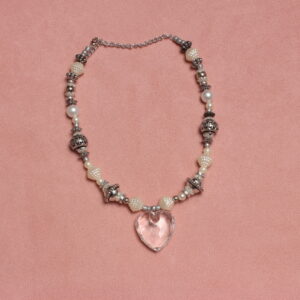 Collier en perles vintage. Alternance de perles blanches nacrées et grises. Pendentif en forme de cœur transparent au centre. Formes et grosseurs variées. Taille ajustable grâce à la chaînette argentée