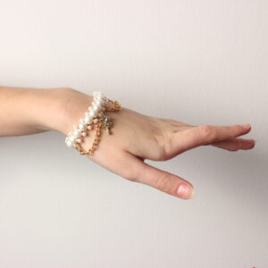 Bracelet élastique en perles vintage. Il est composée de 3 rangées de perles blanches nacrées: 2 rangées de petites perles et une plus grosse au centre. Il est rehaussé de chaînettes dorées et une breloque en forme de clé dorée ornée d'une pierre parme étincelante.