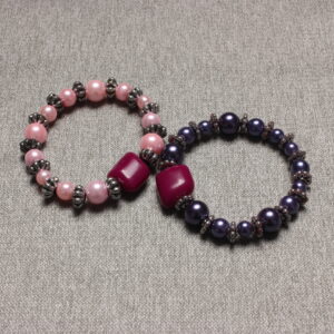 2 bracelets en perles vintage. Un avec une alternance de perles roses pâles et d'intercalaires argentés et la'autre avec les mêmes intercalaires argentés et des perles violettes. Tous 2 rehaussés d'une grosse perle grenat de forme proche du cube. A partager avec sa meilleure amie ou à garder les 2 pour soi