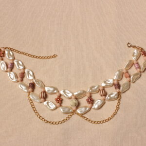 collier tour de cou vintage. Double rangée de perles beiges nacrées en forme de coquillage reliées entre elles par des perles fantaisies fleurs en imitation bois. 2 chaînettes pendantes dorées forment des arcs de cercle. Taille ajustable grâce à la chaînette dorée à l'arrière