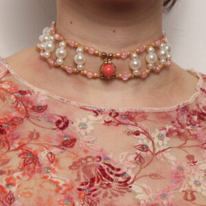 Collier ras le cou en perles vintage. 2 rangées de perles rose reliées entre elles par des petites rangées de 3 perles verticales blanches nacrées. Au centre il y a un pendentif doré orné d'une perle rose. Taille ajustable grâce à la chaînette dorée