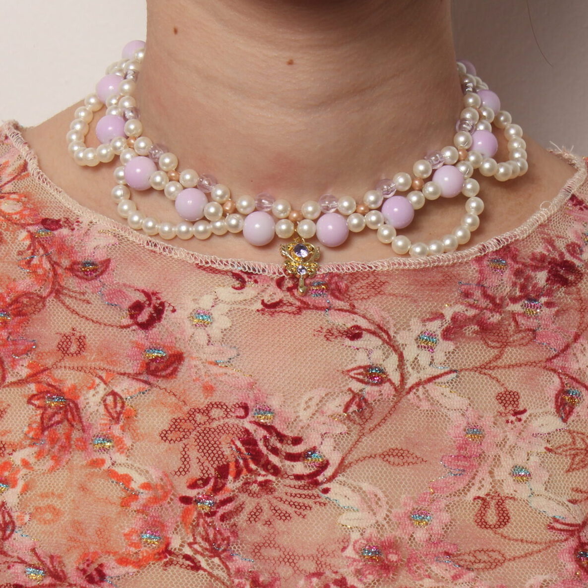 Collier en perles vintage. 2 rangées de perles blanches et parme, composées de petites perles pour la rangée la plus près du cou et de perles parme plus grosses pour la seconde rangée. Arcs de cercles en perles blanches nacrées pour donner du relief au collier. Pendentif doré en forme de clé avec une pierre étincelante parme au centre.