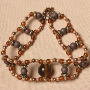 Tour de cou vintage en perles: marron opaques et marron transparentes, dorées, beiges. 2 rangées parallèles de petites perles reliées entre elles par des perles un peu plus grosses. Au centre une grosse perle en verre œil de tigre kaki. Taille ajustable grâce à une chaînette dorée