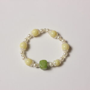 Bracelet élastique vintage composé d'une alternance de perles jaunes pâles, blanches nacrées et transparentes. Chaque perle jaune est entourée d'une corolle blanche nacrée. Une magnifique pierre cubique verte vient sublimer le tout