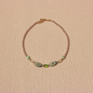 Collier en perles vertes et beiges. Les petites perles beiges se trouvent aux extrémités et sont en verre. Ensuite il y a de chaque côté 2 perles rondes vertes claires striées, puis 2 perles géométriques translucides, 2 perles ovales de taille moyenne, en résine vertes avec des motifs fleurs plus claires et au centre une perle verte translucide. Chaînette d'extension dorée à l'arrière.