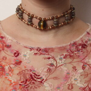 Tour de cou vintage en perles: marron opaques et marron transparentes, dorées, beiges. 2 rangées parallèles de petites perles reliées entre elles par des perles un peu plus grosses. Au centre une grosse perle en verre œil de tigre kaki. Taille ajustable grâce à une chaînette dorée