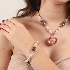 Bracelet et collier en perles. Il y a une alternance de petites perles roses pâles; des moyennes transparentes en forme de goutte, des rondes et des ovales grenat en verre, des grises argentées et des petites rondes transparentes avec des motifs fleurs. Au centre du collier, il y a un pendentif en verre transparent avec un centre rose et des petites fleurs peintes. Chaînette d'extension argentée à l'arrière