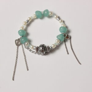 Bracelet en perles. Petites perles blanches nacrées et grises et perles bleues vertes claires translucides en forme de demi cercle qui se font face pour former une sorte de sablier. Au centre une belle breloque grise argentée. De chaque côté 2 breloques en formes de cœur avec des chaînettes argentées tombantes très modernes. Une autre chaînette argentée épouse la forme ronde du bracelet à l'avant au niveau de la breloque centrale ce qui la met en valeur.