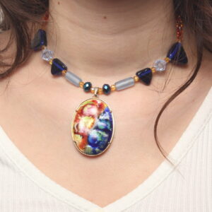 Collier en perles bleues et oranges. Perles triangulaires grosses et petites bleues marines en verre, perles bleues claires en forme de tube en verre. Petites perles géométriques orange en acrylique. Au centre un magnifique pendentif en émail d'un côté orange avec des fleurs jaunes et de l'autre bleu foncé avec des fleurs bleues claires. Chaînette d'extension dorée.