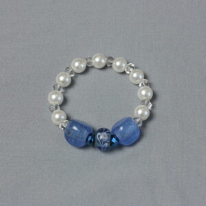 Bracelet en perles de verre. Il est composé d'une alternance de perles moyennes blanches nacrées et de petites transparentes. Il est rehaussé de 2 grosses perles triangulaires bleues lavandes en verre de Murano, de 2 petites perles à facettes d'un bleu plus soutenu et au centre une perle de verre bleu lavande avec des motifs peints en blanc de forme arrondie.