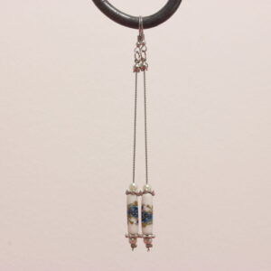 Boucles d'oreilles vintage montées sur des apprêts en acier inoxydable argenté. Magnifique perle en céramique en forme de tube où sont peintes des fleurs bleues au feuillage vert. Elles sont entourées d'intercalaires argentés plats en forme de fleur et de petites perles de verre blanches nacrées.