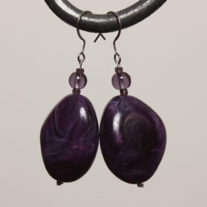 Boucles d'oreilles montées sur des apprêts argentés en acier inoxydable. Grosse perle en forme de galet violette foncée irisée de parme. Au-dessus se trouve une perle ronde violette transparente en verre.