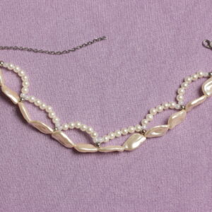 ras de cou composé d'une rangée de perles beiges en forme de coquillages et de perles rondes blanches nacrées formant des demis cercles. A la jonction entre les perles blanches et les beiges se trouvent de petites perles argentées. Chaînette d'extension à l'arrière