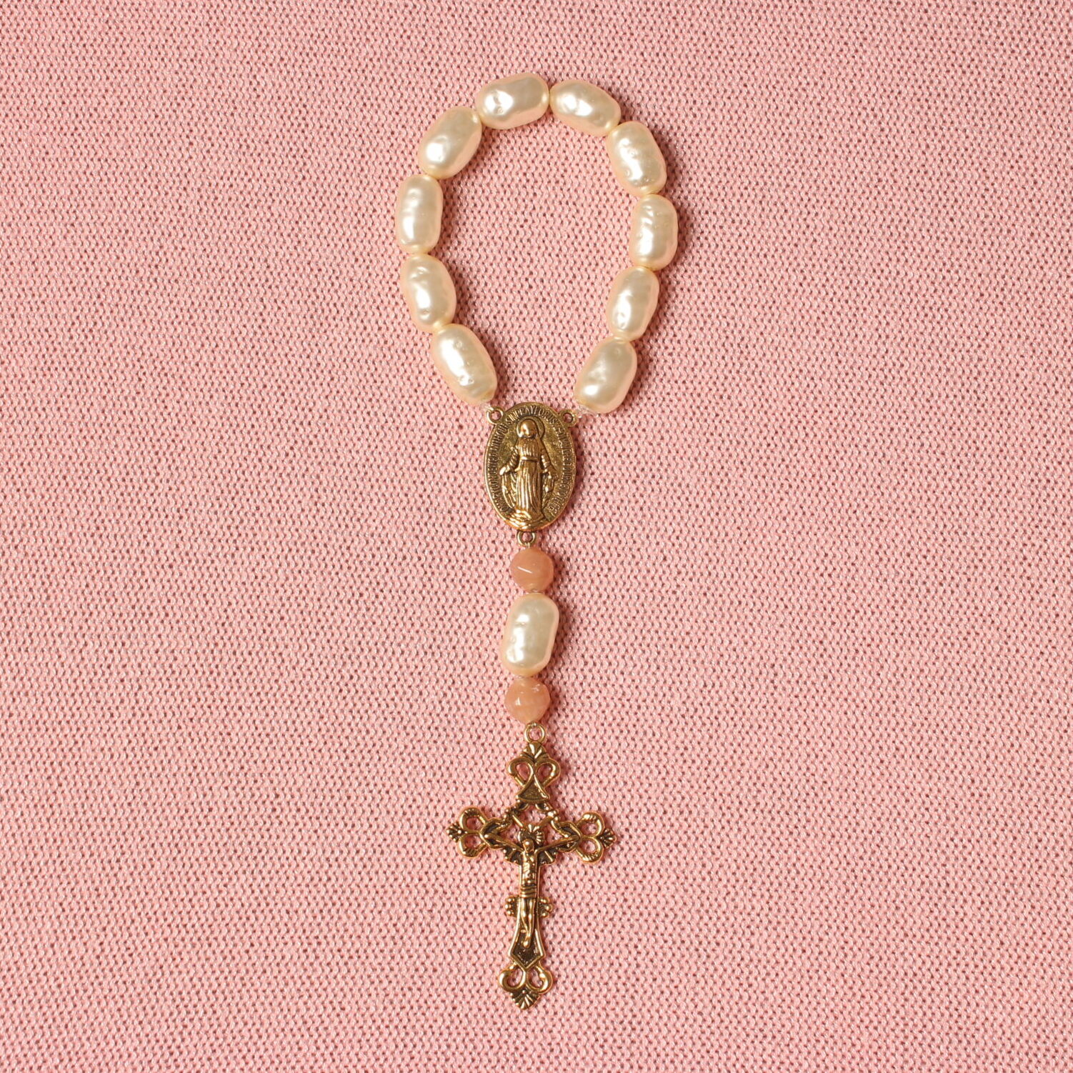 Dizainier composé de perles ovales beiges et de 2 perles roses pâles. Connecteur central et croix en alliage de couleur dorée. Représentation de la vierge Marie sur le connecteur et de Jésus Christ sur la croix