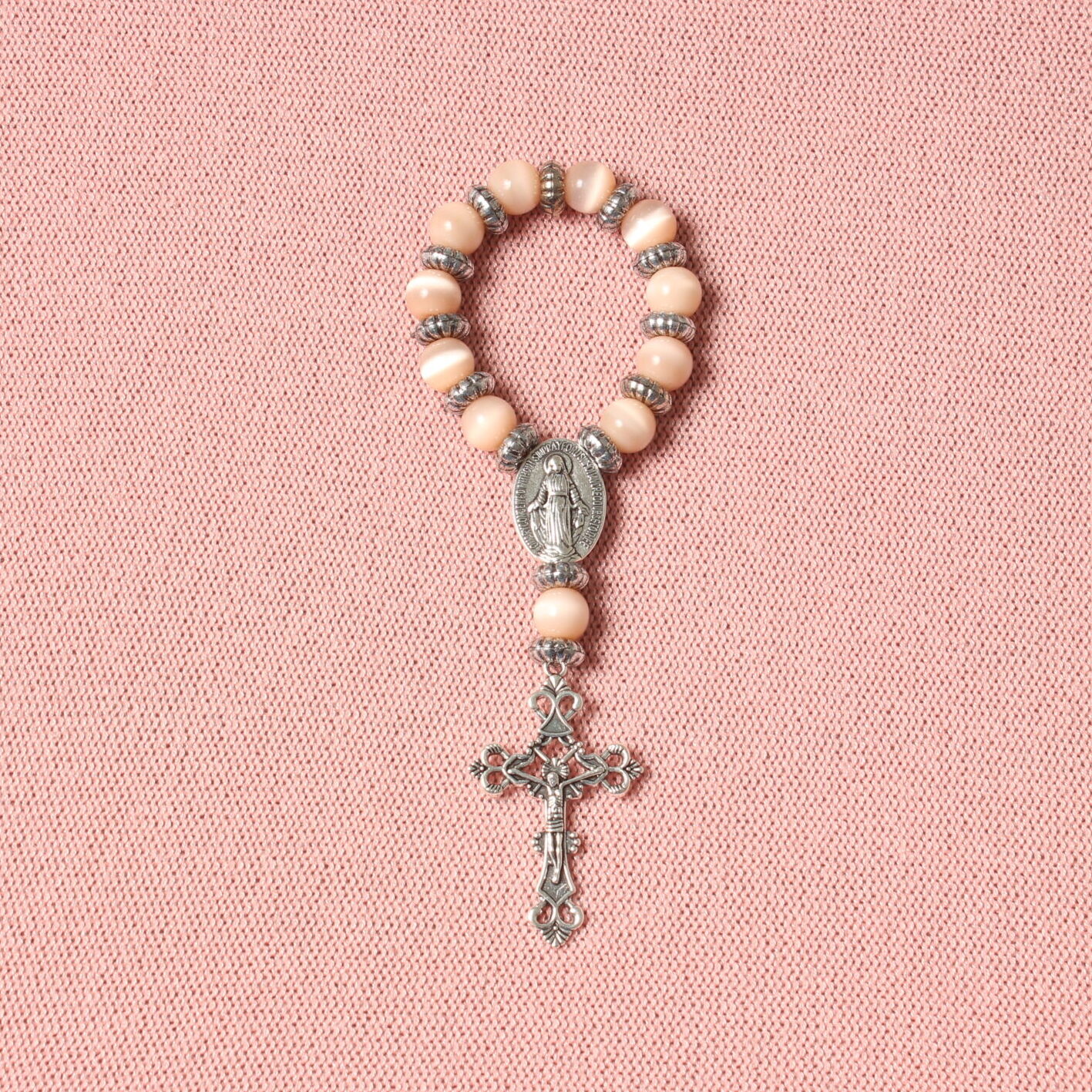 Dizainier composé de perles rondes roses pâles et d'intercalaires argentés. Connecteur central et croix en alliage de couleur argentée. Représentation de la vierge Marie sur le connecteur et de Jésus Christ sur la croix
