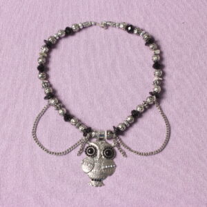 Collier en perles vintage. Alternance de perles noires et grises argentées. Pendentif en forme de chouette au centre décoré de petites perles noires, grises et blanches. Formes et grosseurs variées des perles. 2 chaînettes argentées verticales de chaque côté du pendentif et 2 autres en demi cercle.