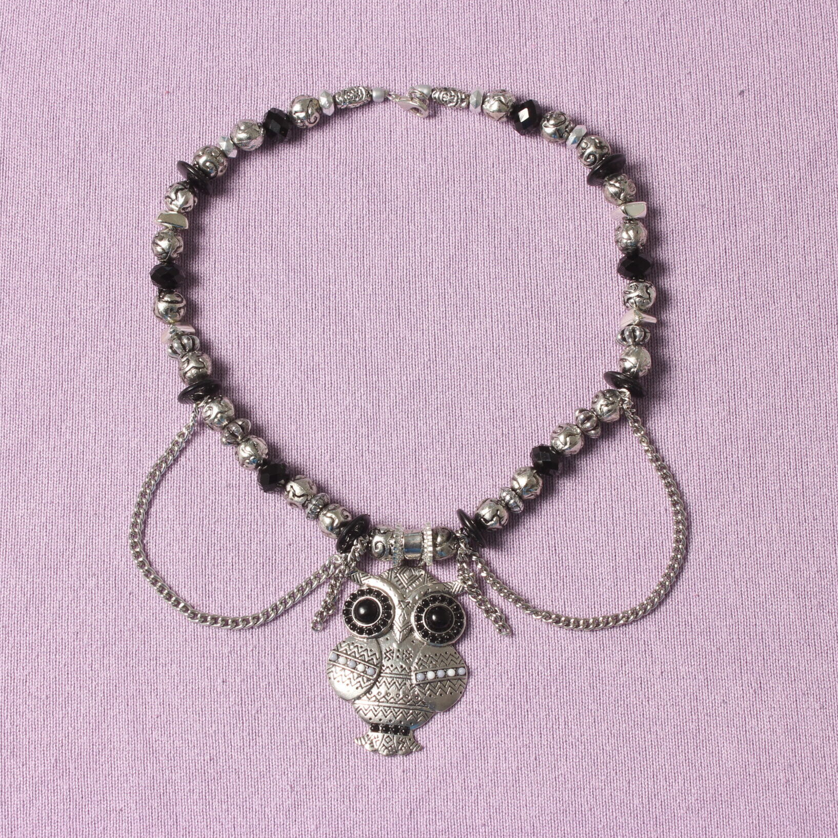 Collier en perles vintage. Alternance de perles noires et grises argentées. Pendentif en forme de chouette au centre décoré de petites perles noires, grises et blanches. Formes et grosseurs variées des perles. 2 chaînettes argentées verticales de chaque côté du pendentif et 2 autres en demi cercle.