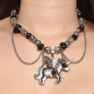 Collier en perles vintage. Alternance de perles noires et grises argentées. Pendentif en forme de licorne au centre décoré de perles noires et grises et de strass. Formes et grosseurs variées des perles. 2 chaînettes argentées verticales de chaque côté du pendentif et 2 autres en demi cercle.