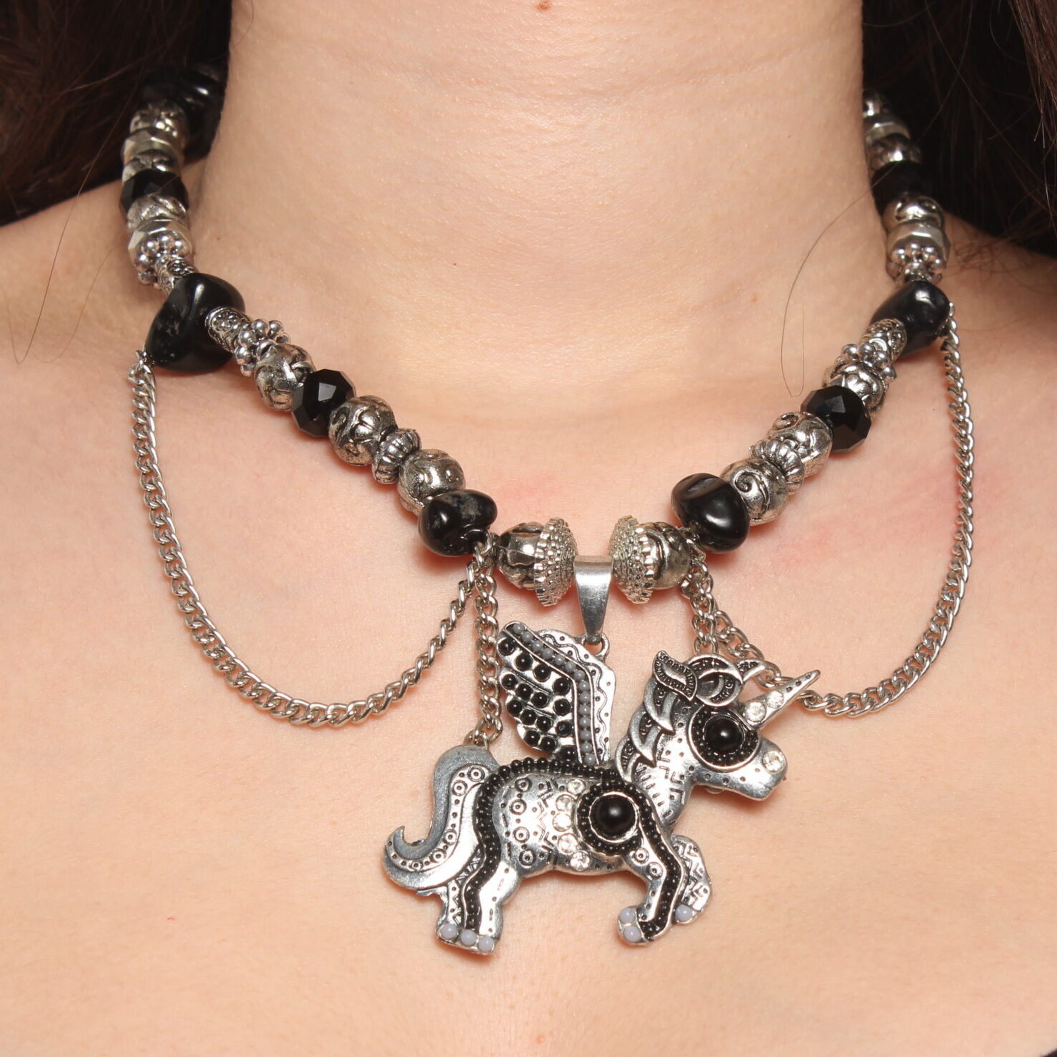 Collier en perles vintage. Alternance de perles noires et grises argentées. Pendentif en forme de licorne au centre décoré de perles noires et grises et de strass. Formes et grosseurs variées des perles. 2 chaînettes argentées verticales de chaque côté du pendentif et 2 autres en demi cercle.