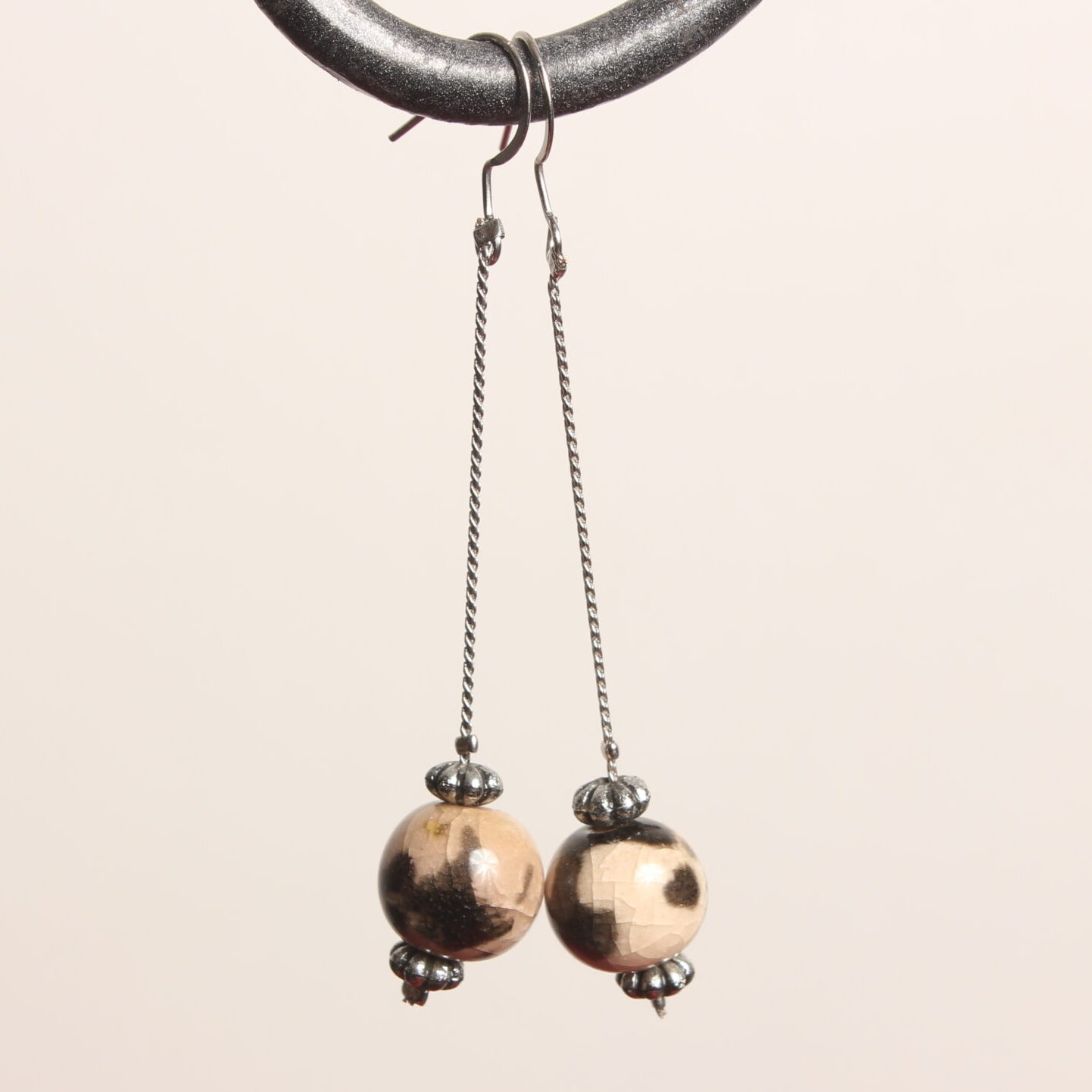Boucles d'oreilles pendantes. Les apprêts argentés sont en acier inoxydable. Une magnifique perle ronde en pierre est suspendue à une fine chaînette argentée. Des motifs léopard sont peints sur la perle. 2 intercalaires argentés sont situés au dessus et au dessous de cette perle. Elle est recouverte d'un vernis transparent lui donnant un effet craquelé
