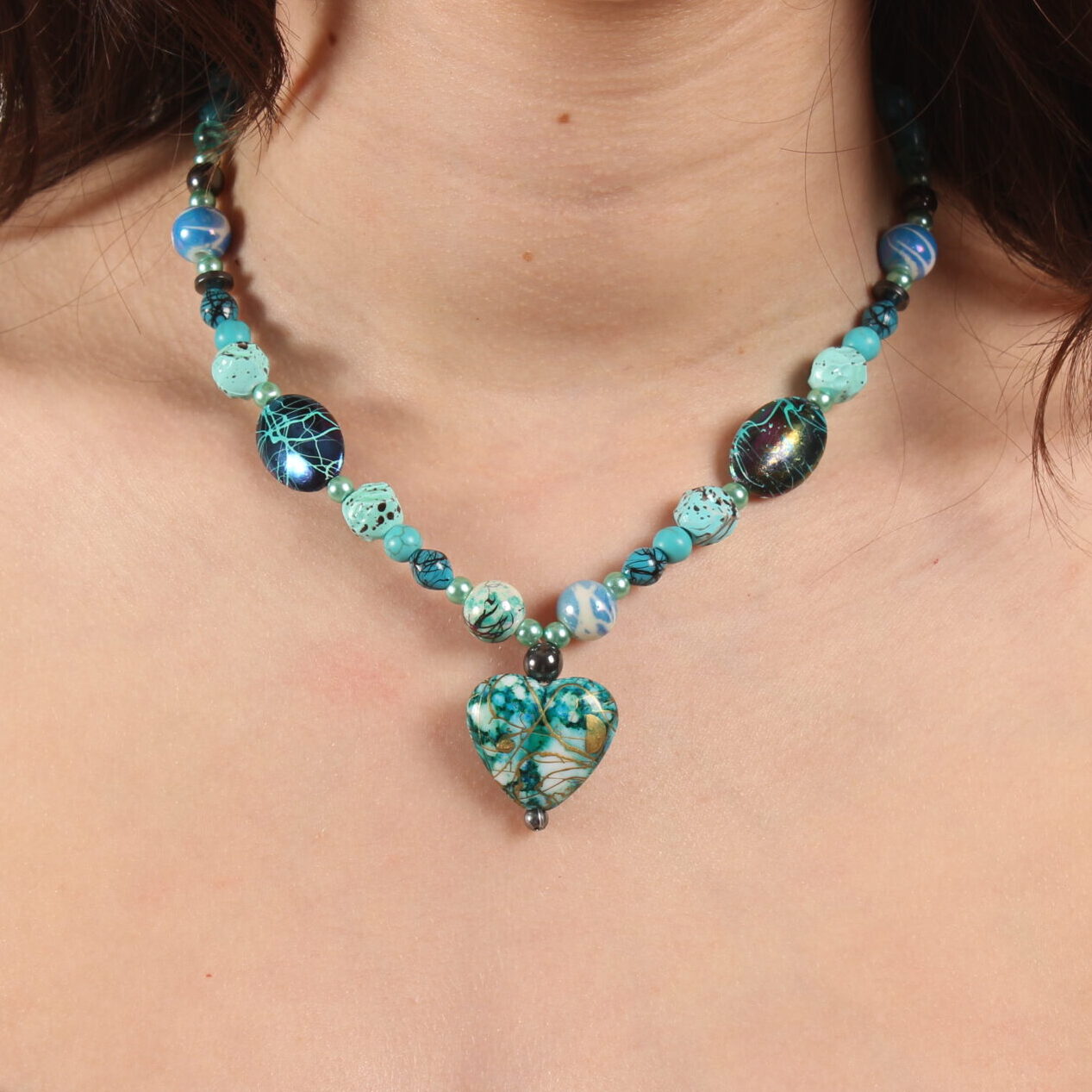 Collier en perles bleues turquoises rondes et ovales de grosseurs variées. Au centre se trouve un magnifique pendentif bleu turquoise en forme de cœur. Chaînette d'extension argentée à l'arrière.