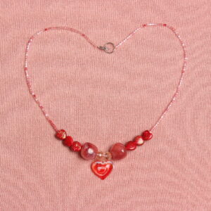 Collier composé de chaque côté de 3 petites perles en forme de cœur, 1 grosse perle rouge rosée, 1 perle en verre transparente et au centre un pendentif en verre rouge et blanc en forme de cœur.