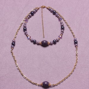 Collier double rangs composé d'un ras du cou et un collier long. Le ras du cou est composé d'une déclinaison de perles violettes et parme où viennent s'intercaler de petites étoiles. Quant au collier long, il est créé autour d'une chaîne dorée sur laquelle se trouve un rappel de 6 perles violettes et parme. Ils sont tous deux agrémentés d'une magnifique perle en pierre violette upcyclée enveloppée de 2 intercalaires dorés. Chaînette d'extension dorée à l'arrière.