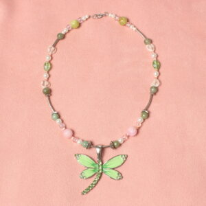 Ce collier possède un pendentif vert avec des strass en forme de libellule. Il est posé sur une longue perle argentée légèrement arrondie. Il est entouré de deux intercalaires légèrement arrondis vers l’extérieure qui englobent une petite perle verte. Elles sont suivies d'une plus petite perle nacrée blanche puis une transparente en finissant par une toute petite perle rose œil de chat. Toutes ces perles en symétrie autour d'une plus grosse perle en pierre rose. Ensuite une autre intercalaire argentée carrée englobe la petite perle verte. Elle est suivie d'une autre perle longue exactement comme celle qui porte le pendentif. Ensuite, il y a une petite intercalaire argentée. Puis, il y a une symétrie autour d'une grosse perle verte en verre qui contient une alternance d'une petite perle verte, d'une perle transparente en forme de cœur, une très petite perle rose œil de chat, une perle transparente, et encore une perle œil de chat. Ensuite, il y a une dernière longue perle argentée. Enfin, il y a une dernière alternance de perle autour d'une grosse perle verte qui est constituée de deux petites perles nacrées et d'une petite perle transparente. tout ça en répété symétriquement autour du gros pendentif. il y a de plus un petit fermoir et un anneau pour fermer le collier.