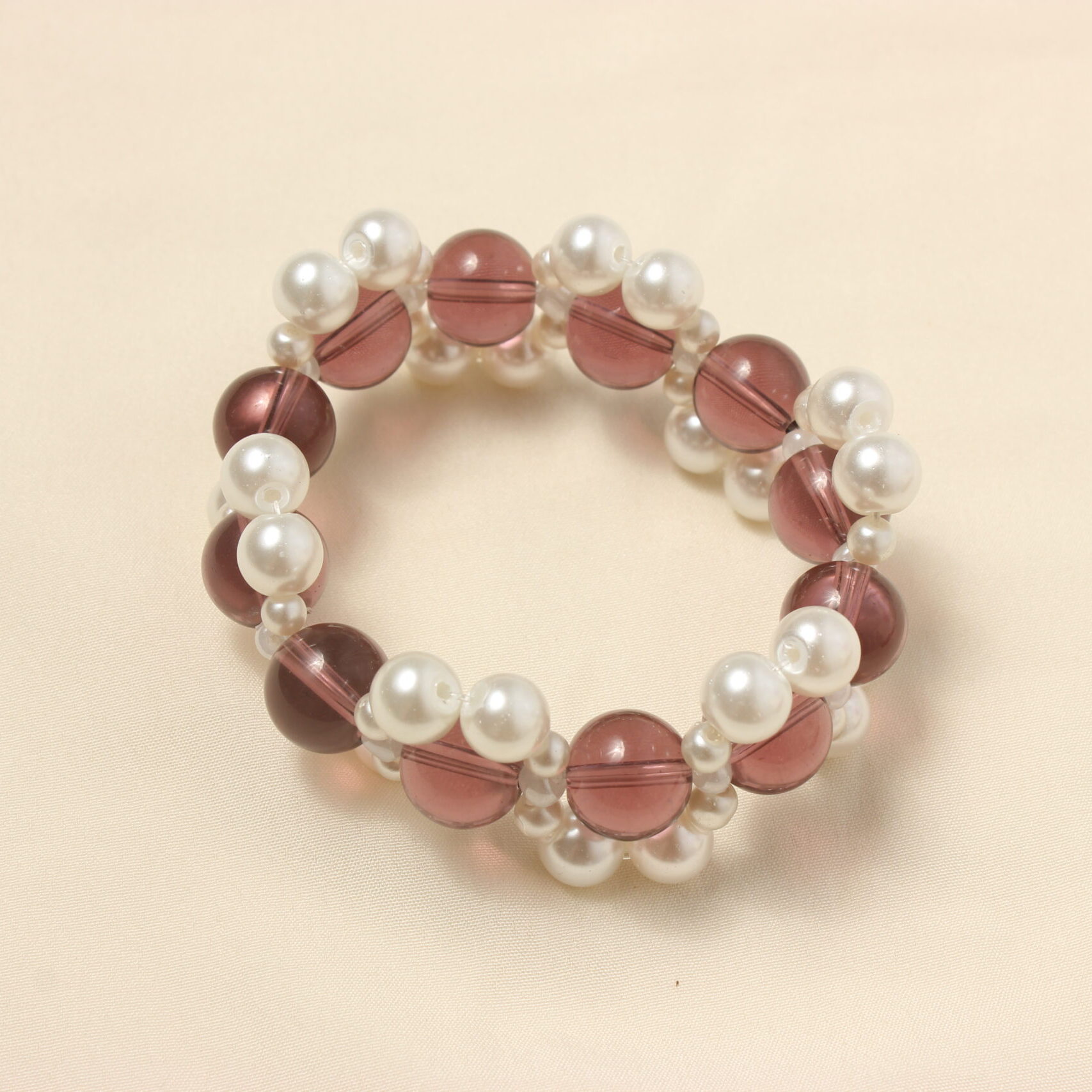 Ce bracelet élastique est constitué de grosses perles en verre violettes entourées de perles plus petites en verre cirée blanches. Les perles blanches sont constituées de deux perles moyennes puis de trois perles plus petites. Elles entourent les perles violettes d'un seul coté. (en haut puis en bas, créant un effet de vague autour des perles violettes.)