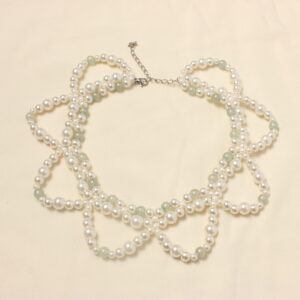 ce collier entièrement en verre est constitué de trois rangées. Deux très rapprochées en ras du cou et une troisième plus grande formant des demi cercles. Ce collier possède une alternance de perles nacrées blanches et de perles bleues/ grises. Ainsi qu'une autre alternance entre des perles nacrées blanches plus ou moins grosses. Ce bijou se ferme grâce à un petit fermoir et à une petite chaînette.