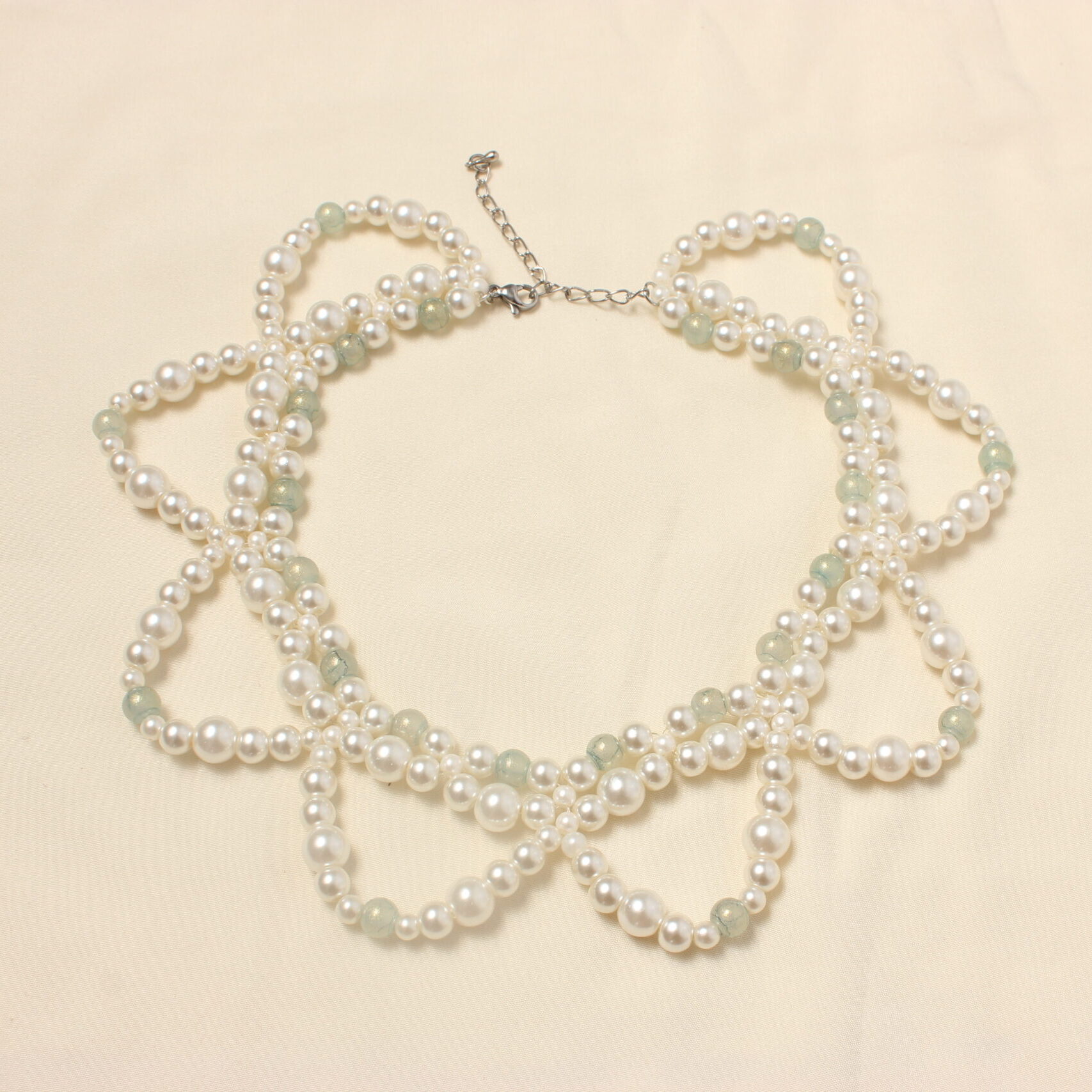 ce collier entièrement en verre est constitué de trois rangées. Deux très rapprochées en ras du cou et une troisième plus grande formant des demi cercles. Ce collier possède une alternance de perles nacrées blanches et de perles bleues/ grises. Ainsi qu'une autre alternance entre des perles nacrées blanches plus ou moins grosses. Ce bijou se ferme grâce à un petit fermoir et à une petite chaînette.
