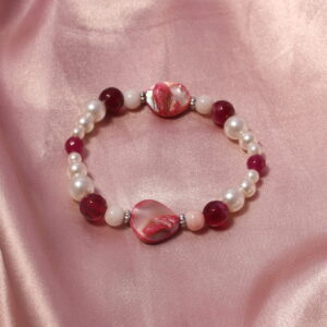Ce bracelet est composé, à chaque extrémité, de perles roses et blanches nacrées aux formes asymétriques. Autour de celles-ci se trouve une alternance de perles violettes en verre ou en pierre, de perles roses en pierre, ainsi que de perles blanches en verre ciré de différentes tailles.