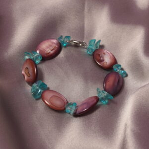 Ce bracelet en verre est constitué d’une alternance de perles ovales violettes et de petites perles plates bleues. Il se ferme à l’aide d’un anneau et d’un fermoir.