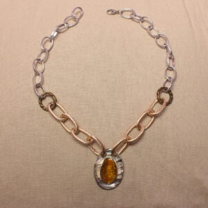 Ce collier est constitué de grosses chaînes autour d’un gros pendentif ovale jaune et argenté avec des petits détails ressemblant à des écailles. La chaîne est argentée à l'extérieur et doré à l'intérieur. Elles sont séparées par des anneaux dorés foncé. Le collier se ferme grace à un fermoir au bout du collier.