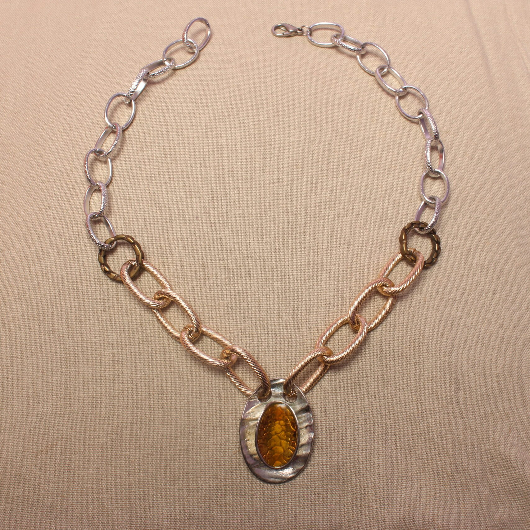 Ce collier est constitué de grosses chaînes autour d’un gros pendentif ovale jaune et argenté avec des petits détails ressemblant à des écailles. La chaîne est argentée à l'extérieur et doré à l'intérieur. Elles sont séparées par des anneaux dorés foncé. Le collier se ferme grace à un fermoir au bout du collier.