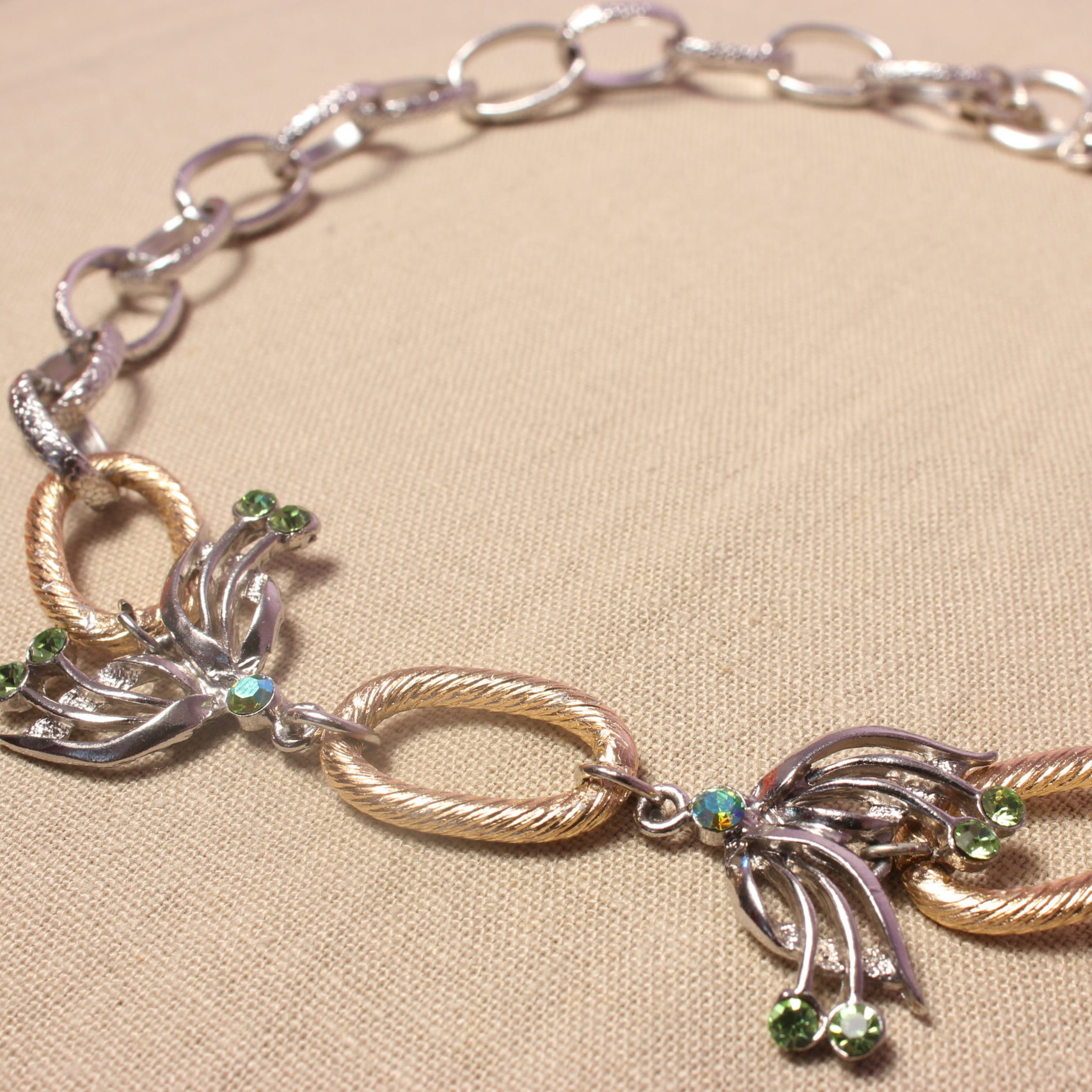 Ce gros collier est constitué de deux pendentifs en forme d’ailes de papillon, ornés de petites strass vertes. Entre ces deux ailes se trouve un anneau doré, qui se retrouve également de l’autre côté des ailes. Une grosse chaîne argentée se poursuit ensuite jusqu’à l’extrémité du collier. Celui-ci se ferme grâce à un fermoir situé au bout de la chaîne.