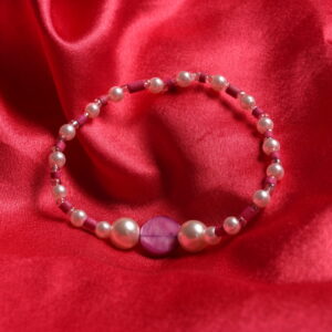 Bracelet composé d'une alternance de petites perles en bois roses fuchsias, en verre roses pâles et en verre blanches. Au centre se trouve une magnifique perle en nacre rose fuchsia ronde plate entourée de 2 perles moyennes en verre roses pâles.