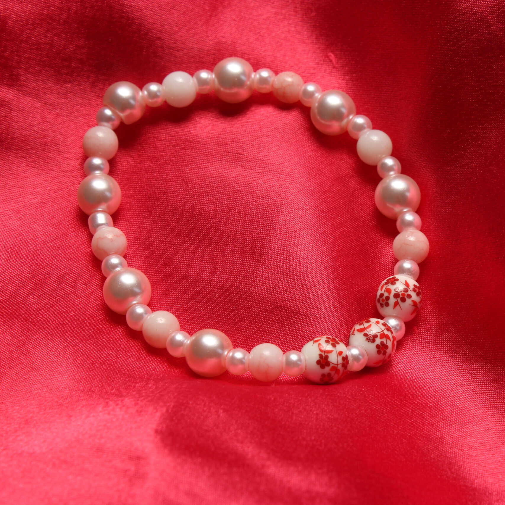 Ce bracelet est composé de perles en verre roses pâles et au centre de 3 perles en céramique blanches sur lesquelles sont peintes des fleurs rouges.