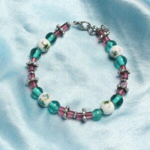 Ce bracelet est constitué d'une succession d'intercalaires en formes de fleur, de perles en tubes roses en verre, de perles bleues et rondes en verre et de perles en céramique avec des motifs floraux bleus. Ce bracelet se ferme grâce à une chaînette et un fermoir argenté.
