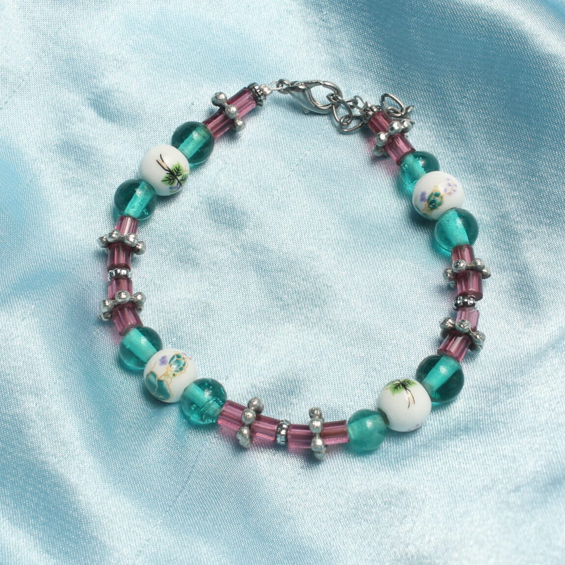 Ce bracelet est constitué d'une succession d'intercalaires en formes de fleur, de perles en tubes roses en verre, de perles bleues et rondes en verre et de perles en céramique avec des motifs floraux bleus. Ce bracelet se ferme grâce à une chaînette et un fermoir argenté.