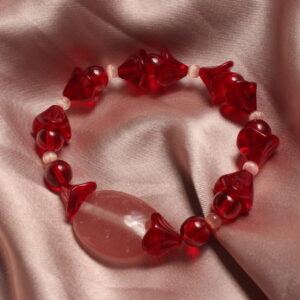 Ce bracelet est constitué d'une grosse perle ovale et rose au centre. symétriquement à cette perle il y a une alternance entre des perles rouges rondes, des perles rouges en formes de fleur et d'autres plus petites œil de chat roses.