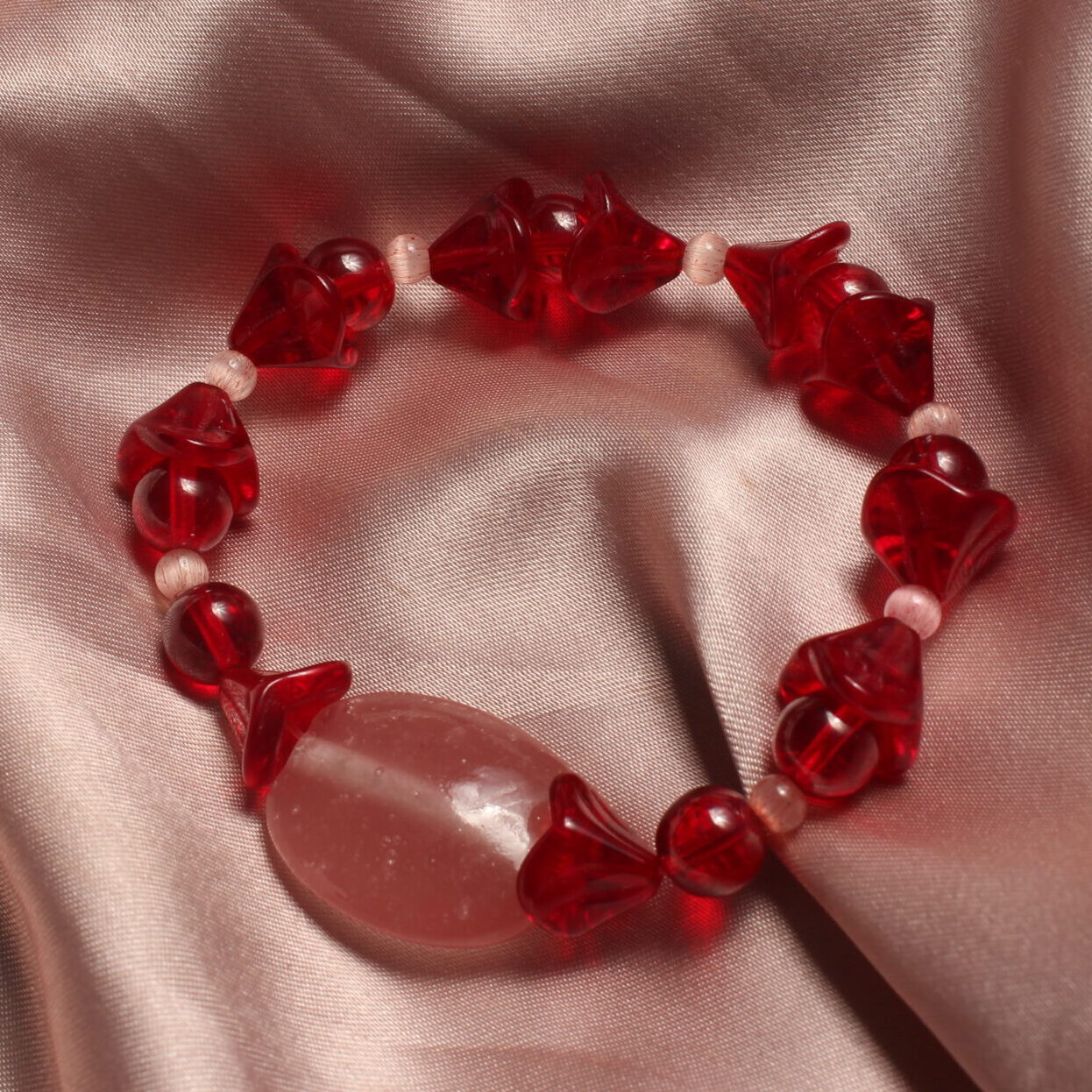 Ce bracelet est constitué d'une grosse perle ovale et rose au centre. symétriquement à cette perle il y a une alternance entre des perles rouges rondes, des perles rouges en formes de fleur et d'autres plus petites œil de chat roses.