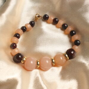 Ce bracelet est constitué de trois grosses perles centrales beiges en pierre. Entre chacune de ces perles se trouvent des intercalaires dorés. De chaque côté, deux perles moyennes en pierre marron viennent compléter l’ensemble. Le bracelet se poursuit ensuite avec une alternance de perles rondes en pierre marron et de perles beiges en pierre, aux formes aplaties. Le bracelet se ferme à l’aide d’un anneau et d’un fermoir doré.