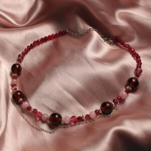 Ce collier est constitué d'une succession de perles en verre de différentes taille et couleur. Il y a des grosses perles marron et des plus petites avec des tons de rose différents. Il possède également un petite chaîne qui pend légèrement.
