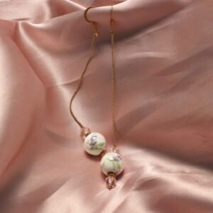 Ces boucles d'oreilles sont constituées d'un fil doré ainsi que trois perles. deux roses en verres autour d'une plus grosse en céramique avec des détails fleuris roses verts et violets.