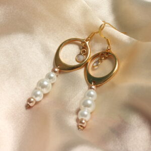 Ces boucles d’oreilles dorées sont constituées d'un anneau doré ainsi qu'in petit pendentif gris en son centre. Des perles nacrées en verres cirées de différentes tailles blanches et dorées pendent légèrement.